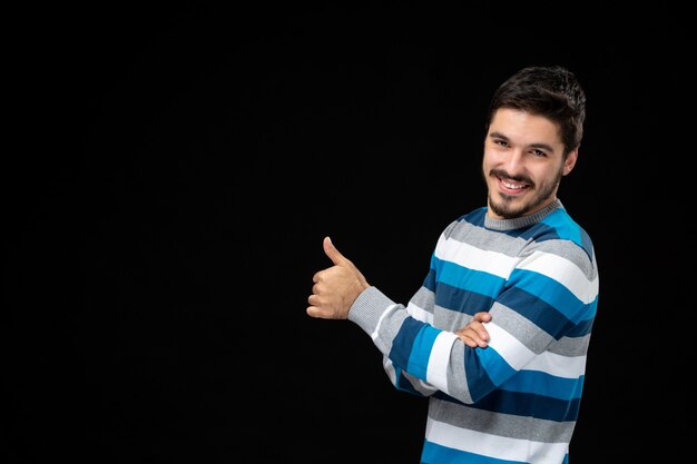 Vue de face jeune homme en jersey rayé bleu sur mur noir modèle photo obscurité couleur humaine