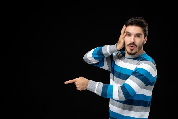 Vue de face jeune homme en jersey rayé bleu sur le mur noir