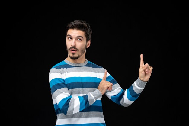 Vue de face jeune homme en jersey rayé bleu sur le mur noir