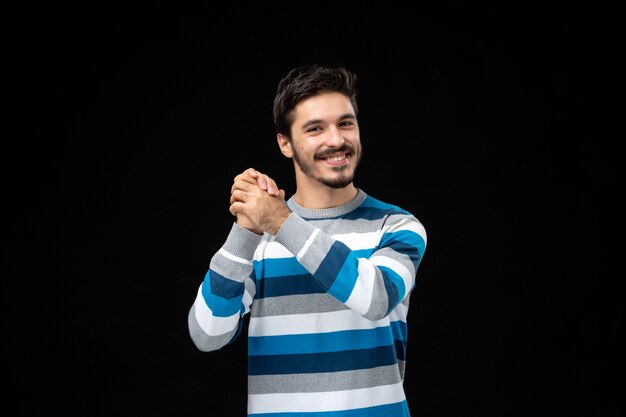 Vue de face jeune homme en maillot rayé bleu souriant sur mur noir