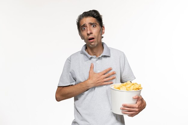 Vue de face jeune homme mangeant des chips de pomme de terre regarder un film sur un bureau blanc