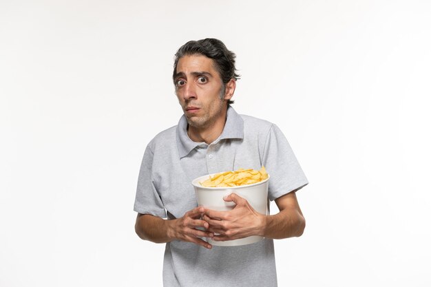 Vue de face jeune homme mangeant des chips de pomme de terre regarder un film sur une surface blanche légère