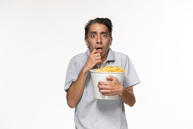 Vue de face jeune homme mangeant des chips de pomme de terre regarder un film sur une surface blanche légère