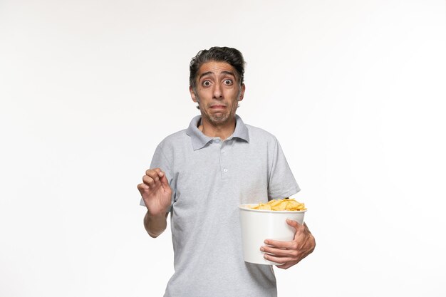 Vue de face jeune homme mangeant des croustilles en regardant un film sur une surface blanche