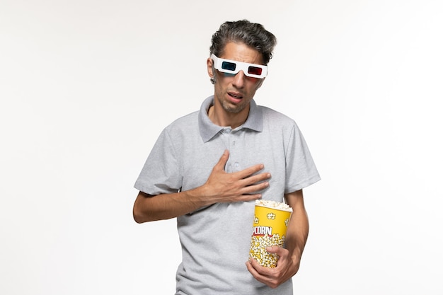 Vue de face jeune homme mangeant du pop-corn dans des lunettes de soleil en regardant un film sur un bureau blanc