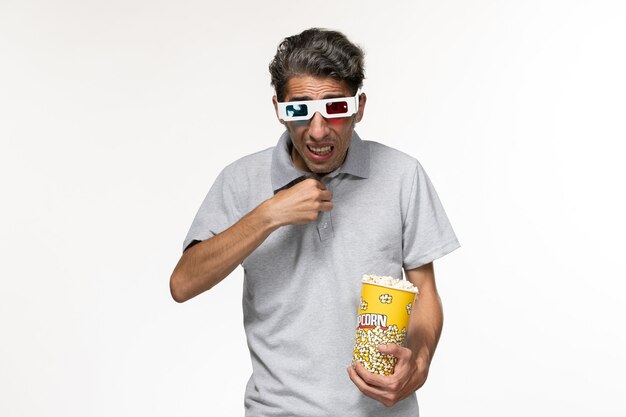 Vue de face jeune homme mangeant du pop-corn dans des lunettes de soleil en regardant un film sur une surface blanche légère