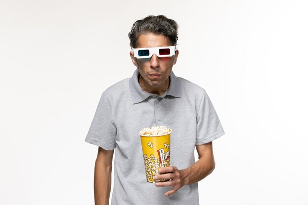 Vue de face jeune homme mangeant du pop-corn dans des lunettes de soleil sur une surface blanche légère