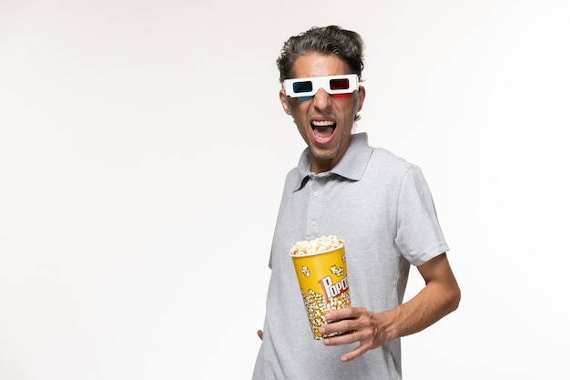 Vue de face jeune homme mangeant du pop-corn dans des lunettes de soleil sur une surface blanche