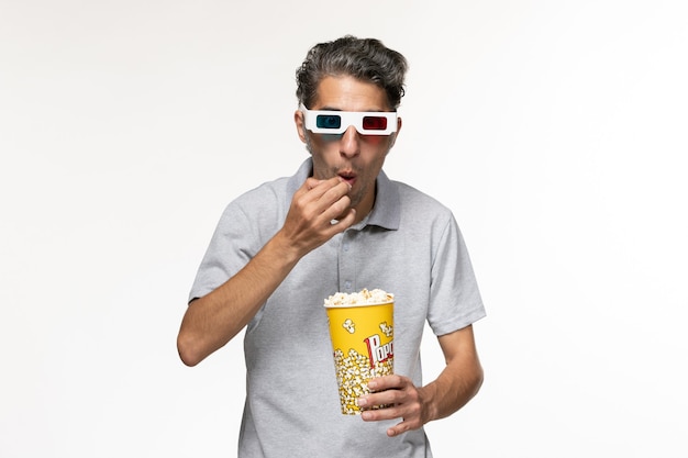 Vue de face jeune homme mangeant du pop-corn dans des lunettes de soleil sur une surface blanche