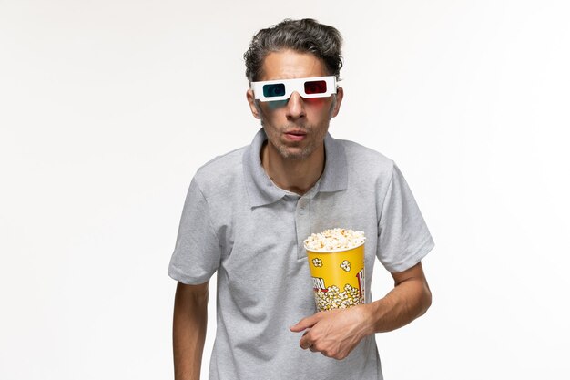 Vue de face jeune homme mangeant du pop-corn dans des lunettes de soleil sur une surface blanche