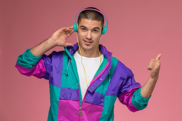 Vue de face jeune homme en manteau coloré, écouter de la musique sur fond rose clair