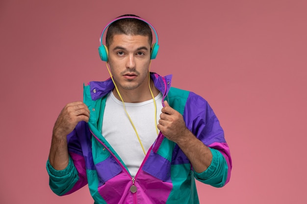 Photo gratuite vue de face jeune homme en manteau coloré posant et écoutant de la musique sur fond rose