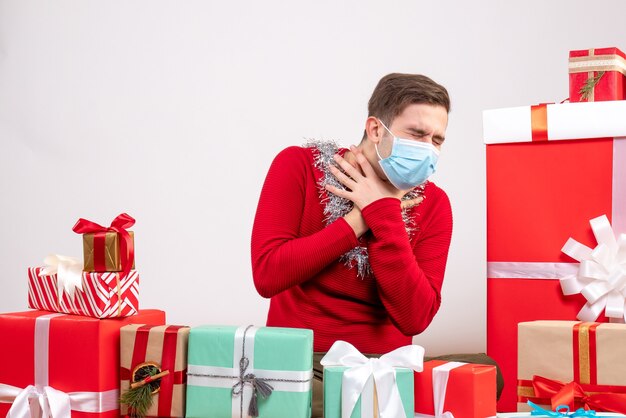 Vue de face jeune homme avec masque fermant les yeux assis autour de cadeaux de Noël