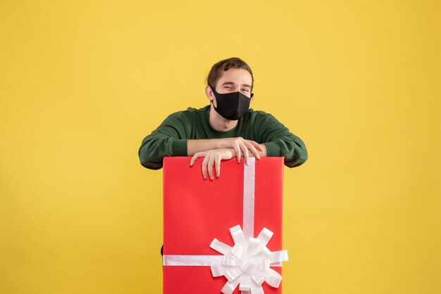 Vue de face jeune homme avec masque noir debout derrière un grand coffret sur jaune