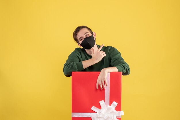 Vue de face jeune homme avec masque noir debout derrière un grand coffret sur jaune