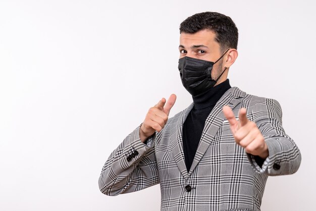 Vue de face jeune homme avec masque noir pointant sur la caméra debout sur fond blanc isolé