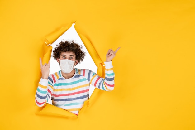 Vue de face jeune homme en masque stérile sur photo de couleur jaune covid- virus de la santé humain