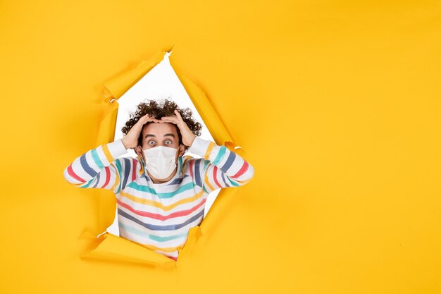 Vue de face jeune homme en masque stérile sur photo de virus pandémique covid couleur jaune