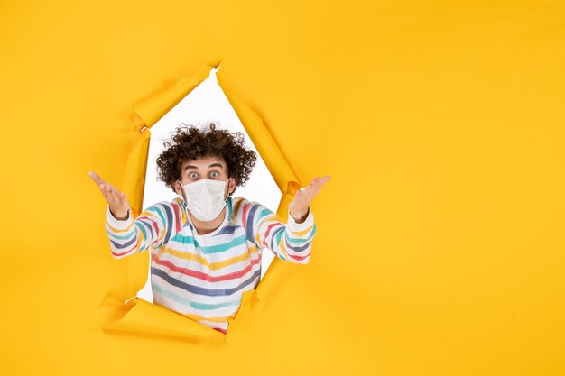 Vue de face jeune homme en masque stérile sur sol jaune santé couleur virus pandémique covid photo humaine