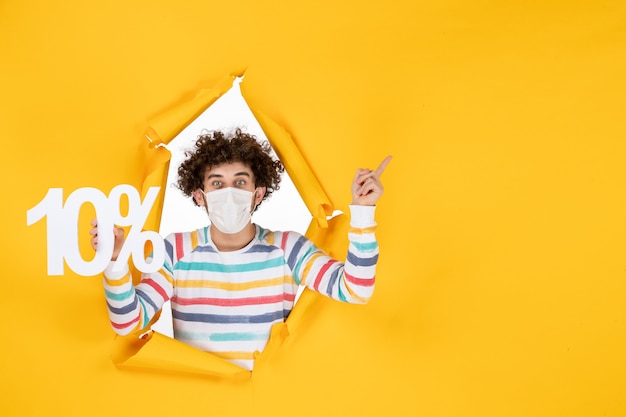 Photo gratuite vue de face jeune homme en masque stérile tenant l'écriture sur photo jaune santé covid vente de pandémie de coronavirus