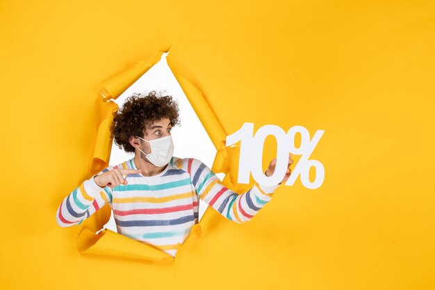 Vue de face jeune homme en masque stérile tenant l'écriture sur photo jaune santé covid vente de pandémie de coronavirus