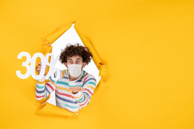 Vue de face jeune homme en masque tenant sur la couleur jaune shopping santé covid- photo vente de virus pandémique