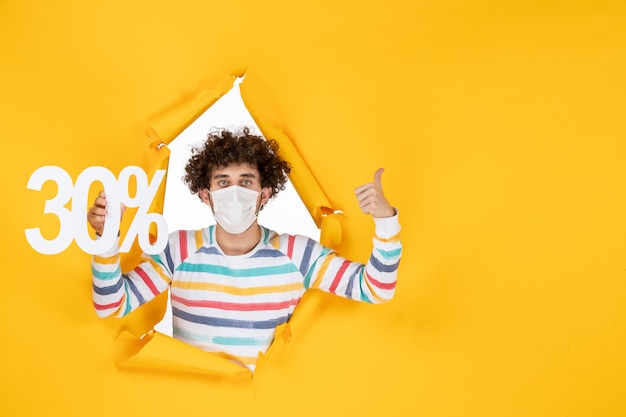 Vue de face jeune homme en masque tenant des couleurs jaunes shopping virus santé covid- photo pandémie