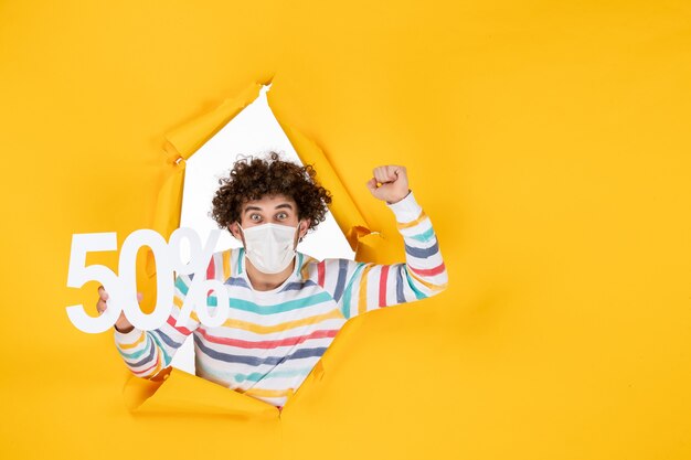 Vue de face jeune homme en masque tenant l'écriture sur le jaune shopping santé pandémie covid- virus photos vente couleur