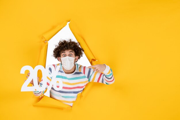 Vue de face jeune homme en masque tenant une écriture sur une photo de pandémie de coronavirus jaune santé covid- couleur de vente