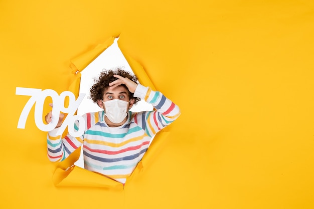 Photo gratuite vue de face jeune homme en masque tenant l'écriture sur le virus de couleur jaune vente covid- photos santé pandémie shopping
