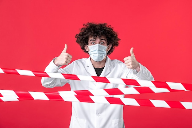 Photo gratuite vue de face jeune homme médecin en uniforme médical et masque sur la bande d'avertissement de danger de quarantaine de l'hôpital d'isolement de fond rouge