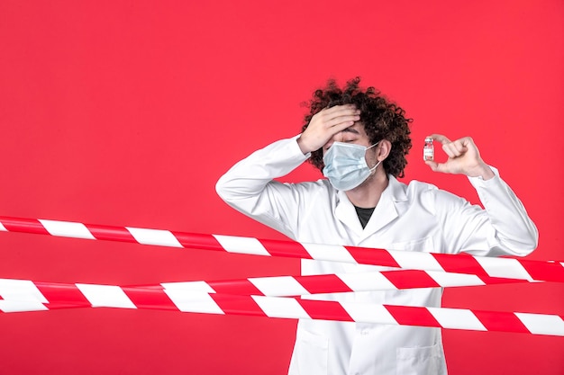 Vue de face jeune homme médecin en uniforme médical tenant une fiole ayant la température sur fond rouge danger hôpital quarantaine covid-bande couleur avertissement santé