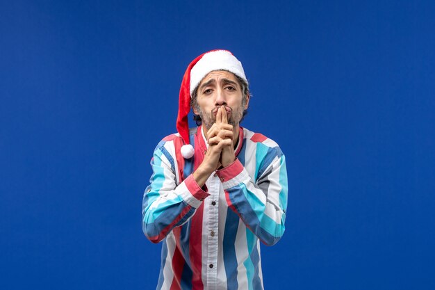 Vue de face jeune homme avec mendicité pose sur bureau bleu noël émotion mâle