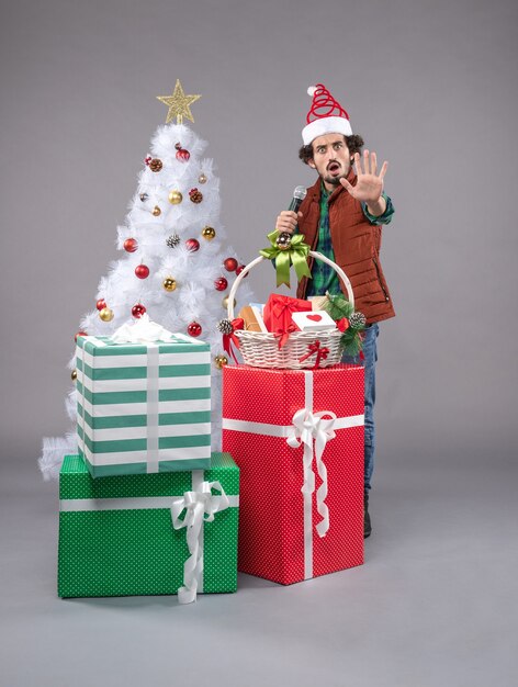 Vue de face jeune homme avec micro autour des cadeaux sur le gris