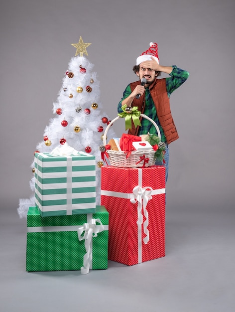 Vue de face jeune homme avec micro autour des cadeaux sur le gris