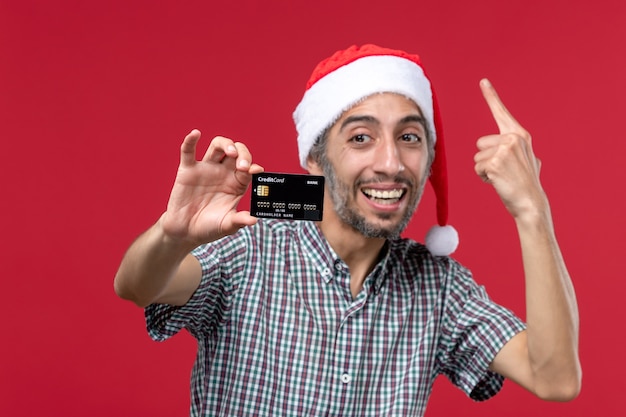 Vue de face jeune homme montrant une carte bancaire sur fond rouge