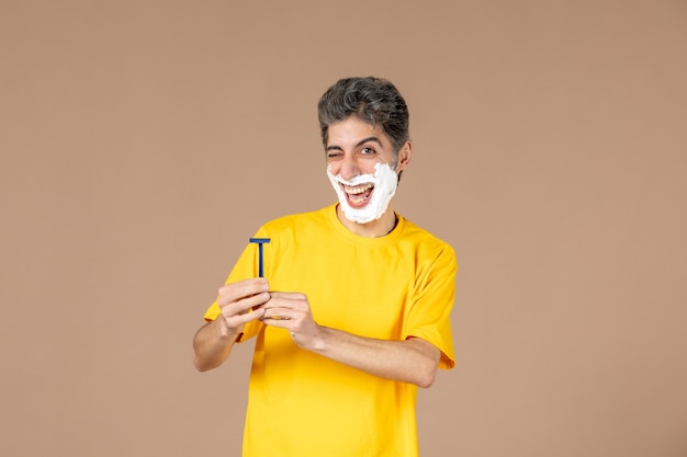 Vue de face jeune homme avec de la mousse sur son visage et un rasoir dans ses mains sur fond rose