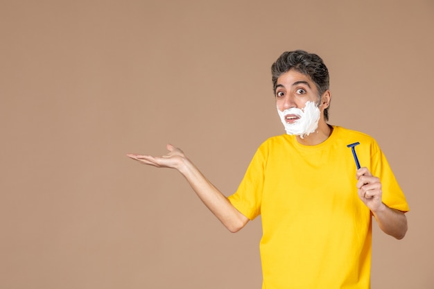 Vue de face jeune homme avec de la mousse sur son visage tenant un rasoir sur fond rose