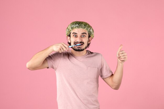 Vue de face jeune homme nettoyant ses dents sur fond rose
