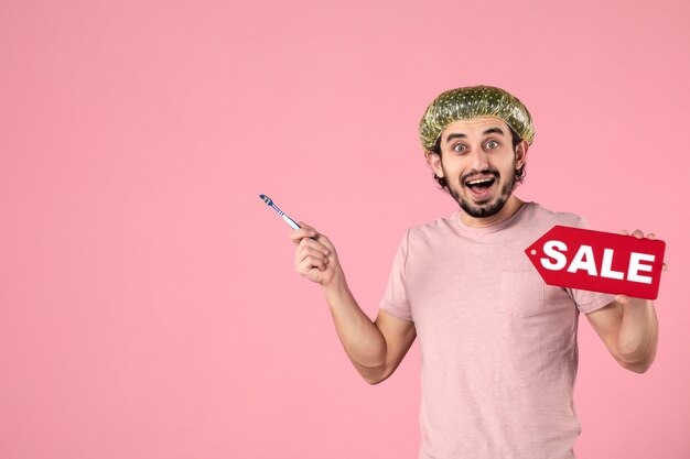 Vue de face jeune homme nettoyant ses dents et tenant la plaque signalétique de vente sur fond rose