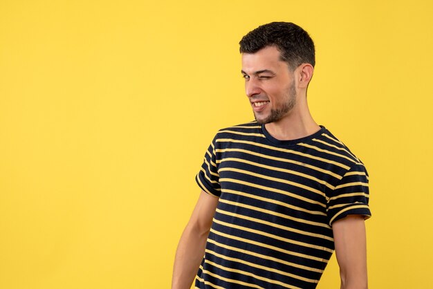 Vue de face jeune homme avec oeil clignotant debout sur fond isolé jaune