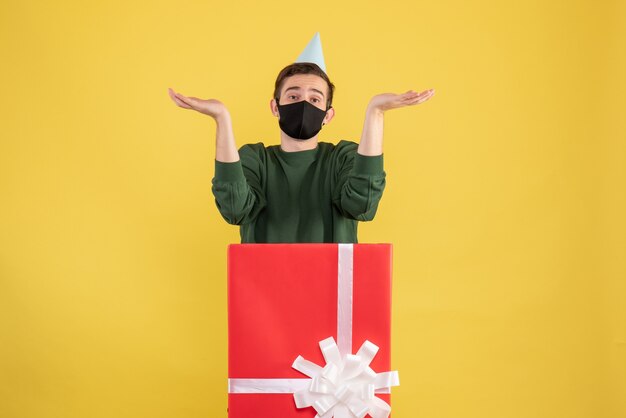 Vue de face jeune homme ouvrant les mains debout derrière un grand coffret sur jaune