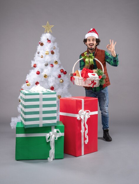 Vue de face jeune homme avec panier autour de cadeaux sur sol gris cadeau de Noël du nouvel an