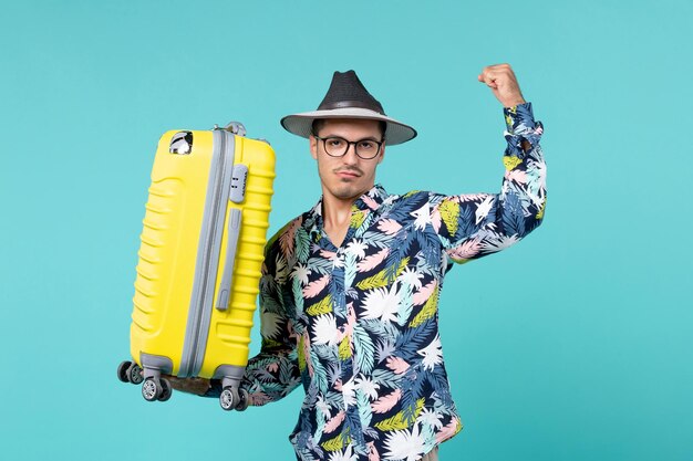 Vue de face jeune homme partant en vacances et tenant son sac jaune sur un bureau bleu