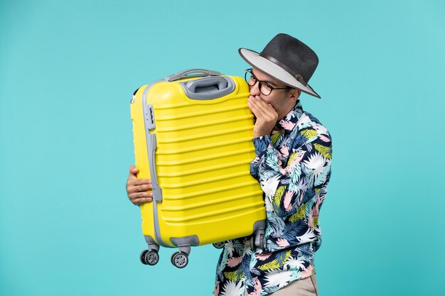 Vue de face jeune homme partant en vacances et tenant son sac jaune sur l'espace bleu clair