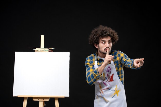 Vue de face jeune homme peintre avec chevalet sur tableau noir