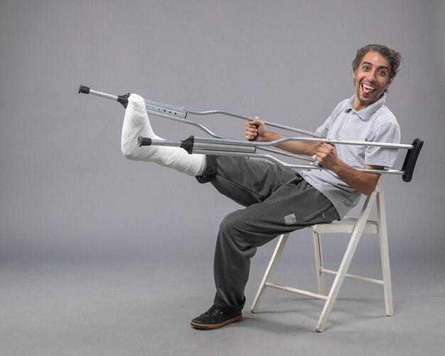 Vue de face jeune homme avec pied cassé à l'aide de béquilles pour marcher sur un mur gris pied cassé torsion accident douleur aux jambes