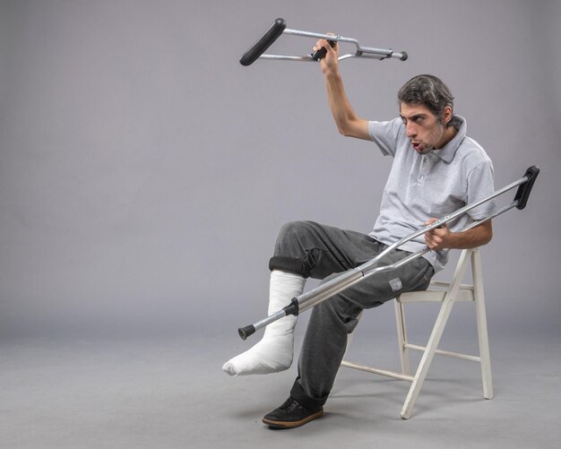 Vue de face jeune homme avec pied cassé à l'aide de béquilles pour marcher sur un pied de bureau gris douleur cassée torsion jambe accident