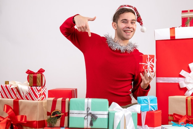 Vue de face jeune homme pointant avec le doigt vers le bas assis autour de cadeaux de Noël