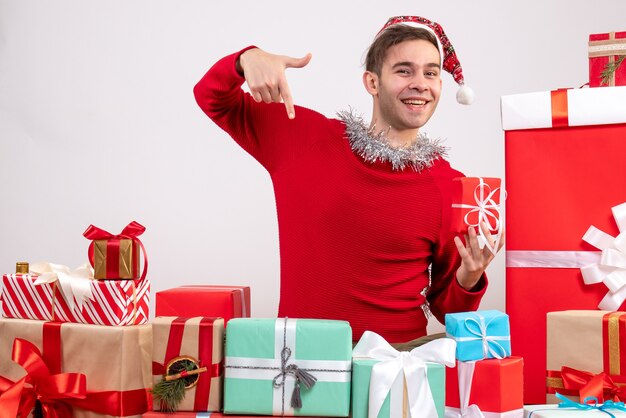 Vue de face jeune homme pointant avec le doigt vers le bas assis autour de cadeaux de Noël